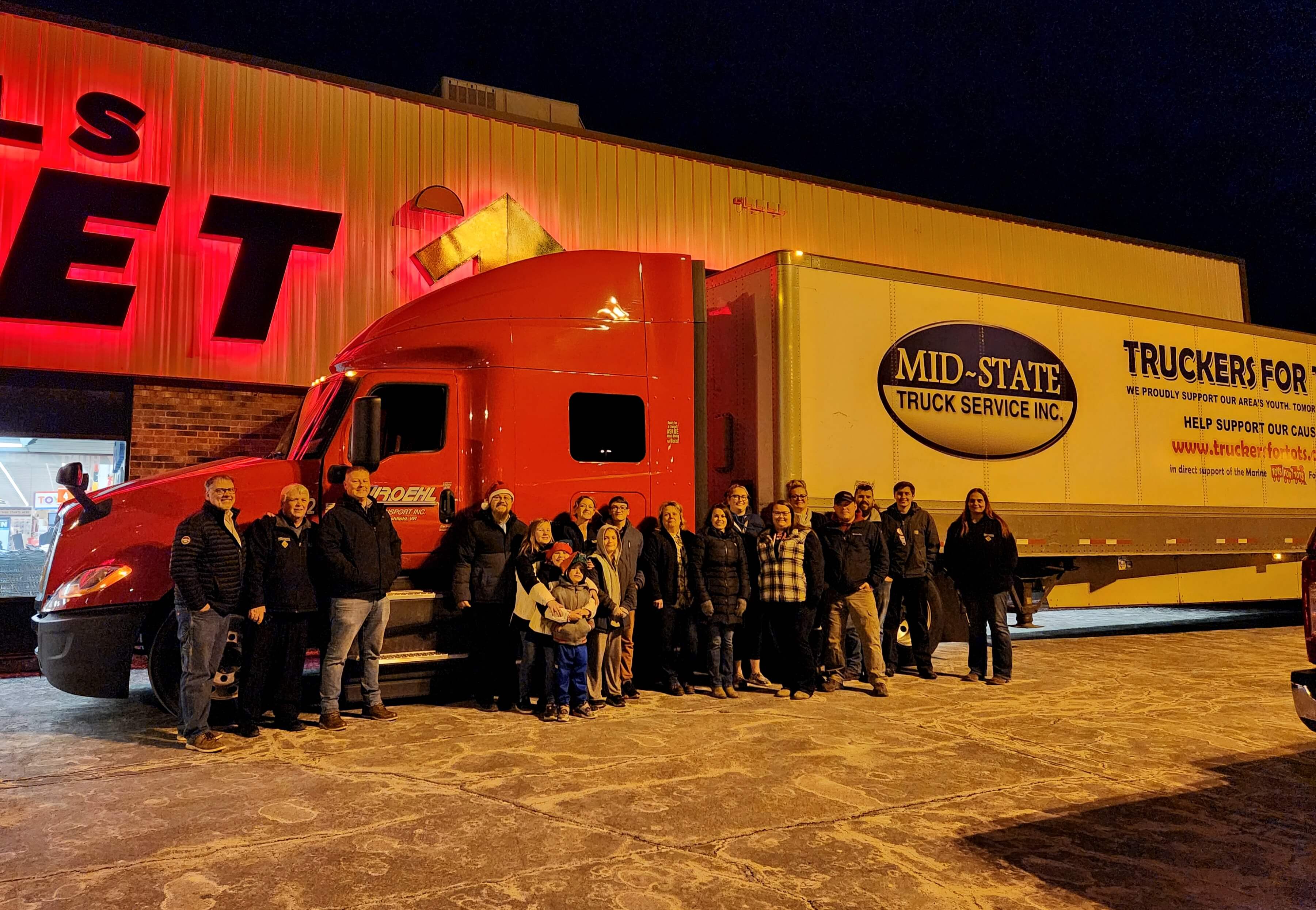 Team beside a Truckers for Tots trailer at night